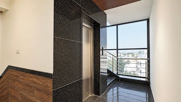 A modern elevator with a glass door, a wooden floor, and a view of a cityscape through large windows.
