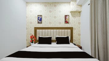 A bedroom with a bed, two pillows, a nightstand, a vase with flowers, and two wall-mounted pictures.