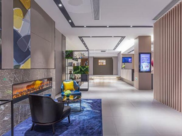 Un moderno vestíbulo de hotel con una zona de estar, una pantalla digital y un mostrador de recepción.