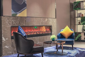 Un área de descanso moderna con chimenea, sillón de cuero, sofá azul y una pequeña mesa con un jarrón.
