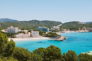 Zona hotelera costera con varios edificios, una playa y aguas azules cristalinas.