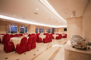 A banquet hall with round tables, red chairs, and a buffet area.