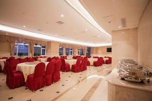 Un salón de banquetes con mesas redondas, sillas rojas y una zona de bufé.