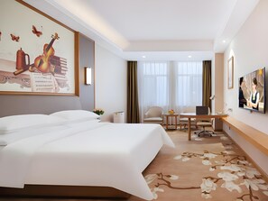Una habitación de hotel con una cama grande, un escritorio con una computadora portátil, una silla y un televisor en la pared.