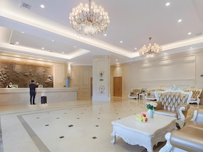 Un vestíbulo de hotel con recepción, candelabros, zona de estar y piso pulido.
