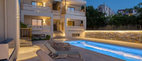 A modern two-story building with a swimming pool and sun loungers.