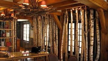 A rustic interior with birch tree branches used as a wall, a wooden desk with a laptop, and a bookshelf.