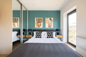 Quarto de hotel moderno com uma cama grande, vista para o exterior e obras de arte na parede.