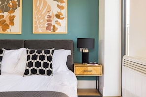 Un dormitorio con una cama, una mesita de noche con lámpara y una obra de arte en la pared.