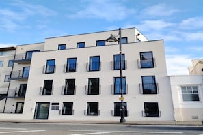 Um edifício moderno de vários andares com fachada plana, janelas uniformemente espaçadas e varandas com grades pretas.