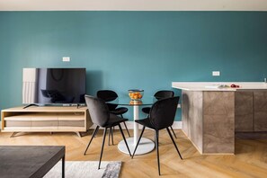 Un espacio habitable moderno con una pared verde azulado, un televisor de pantalla plana, una mesa de comedor con sillas y una zona de cocina con encimera de mármol.