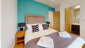 Habitación de hotel con cama, mesitas de noche y baño con lavamanos y espejo.