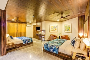 A hotel room with two beds, a desk, a chair, a ceiling fan, and artwork on the walls.