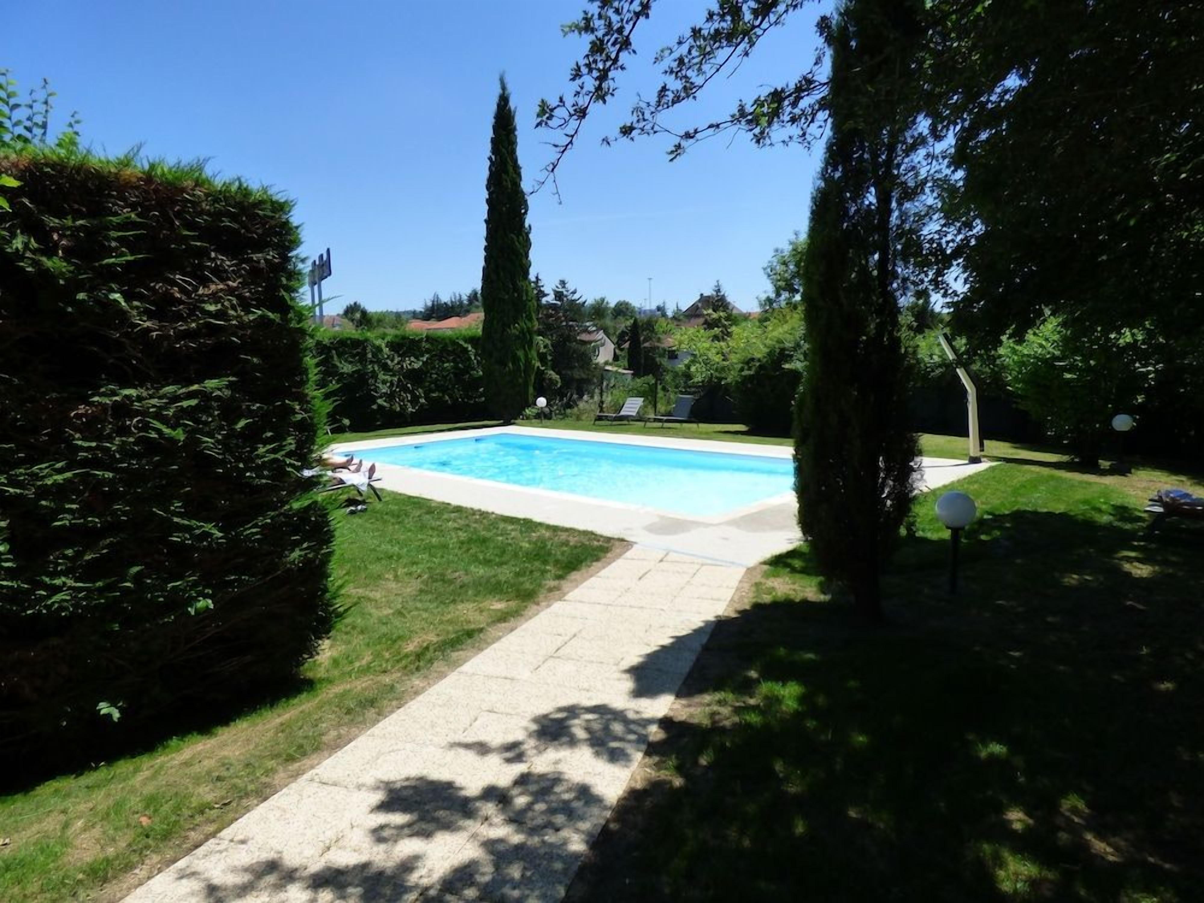 A rectangular swimming pool with a paved walkway leading to it, surrounded by well-maintained grass and hedges.