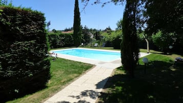 A rectangular swimming pool with a paved walkway leading to it, surrounded by well-maintained grass and hedges.
