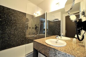 Un bany modern amb taulell de granat, dos rentatolls, un mirall gran i una cabina de dutxa.