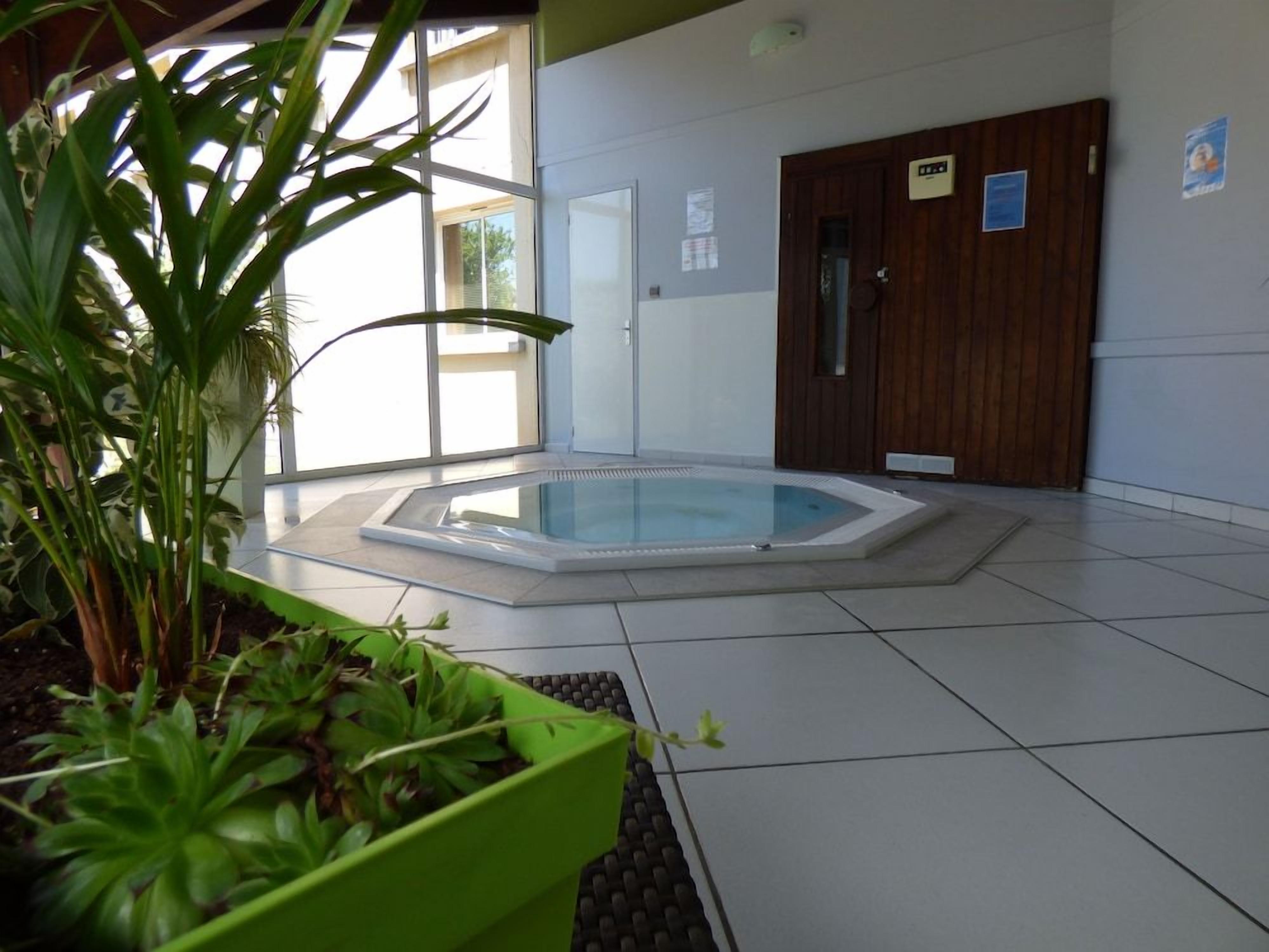 A room with a glass-enclosed hot tub, a wooden door, and a green planter with plants.