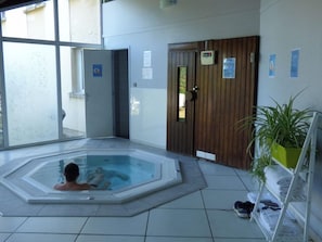 A hot tub in a room with tiled flooring, a wooden door, and a potted plant. - Balladins Villefranche de Rouergue (Villefranche-de-Rouergue)