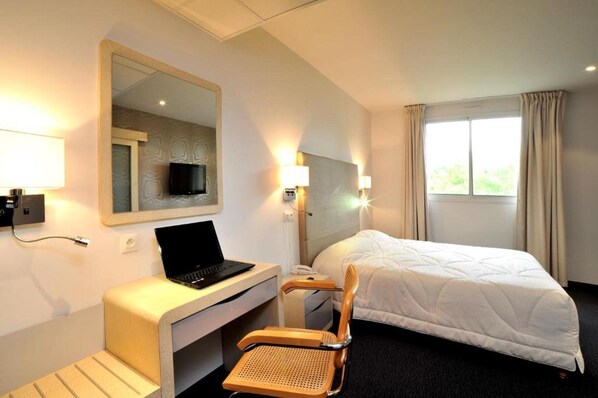 A hotel room with a bed, a desk with a laptop, a chair, a television, and a window with curtains. - Balladins Villefranche de Rouergue (Villefranche-de-Rouergue)