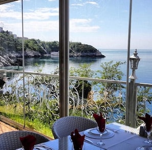 Comedor con una mesa dispuesta para dos, con vista a una masa de agua y un litoral rocoso.
