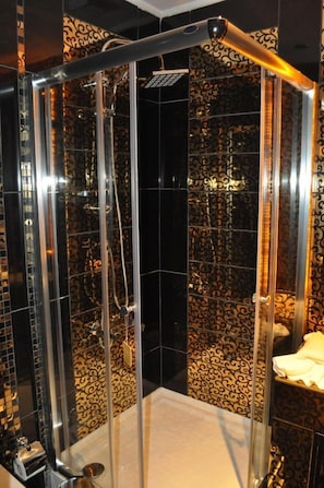 A glass-enclosed shower with a black and gold patterned wall.