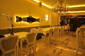 A dining area with a long table, multiple chairs, a chandelier, and a decorative mirror.