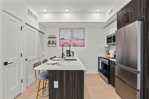 A modern kitchen with a central island, dark wood cabinets, stainless steel appliances, and a view of the sunset through a window. - Stylish Apartment w Parking | Museums • Center City (Philadelphia)