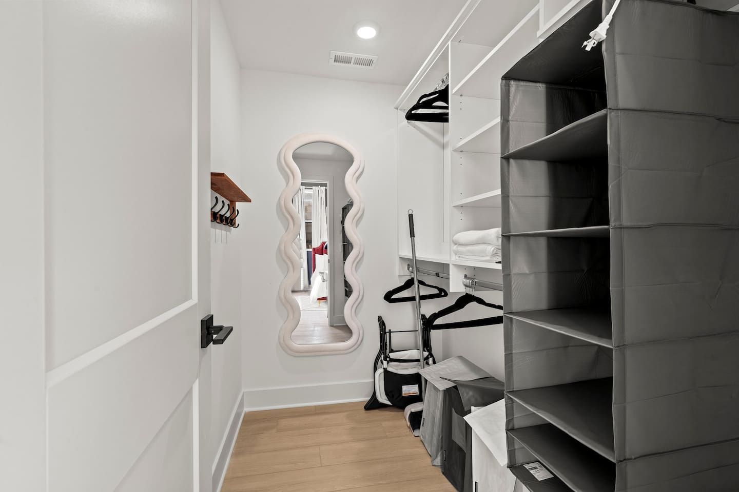 A hallway with a mirror, a coat rack, and a storage unit with shelves.