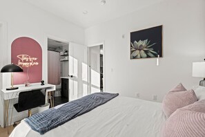Un dormitorio moderno con cama, mesita de noche, lámpara y un letrero de neón en la pared.
