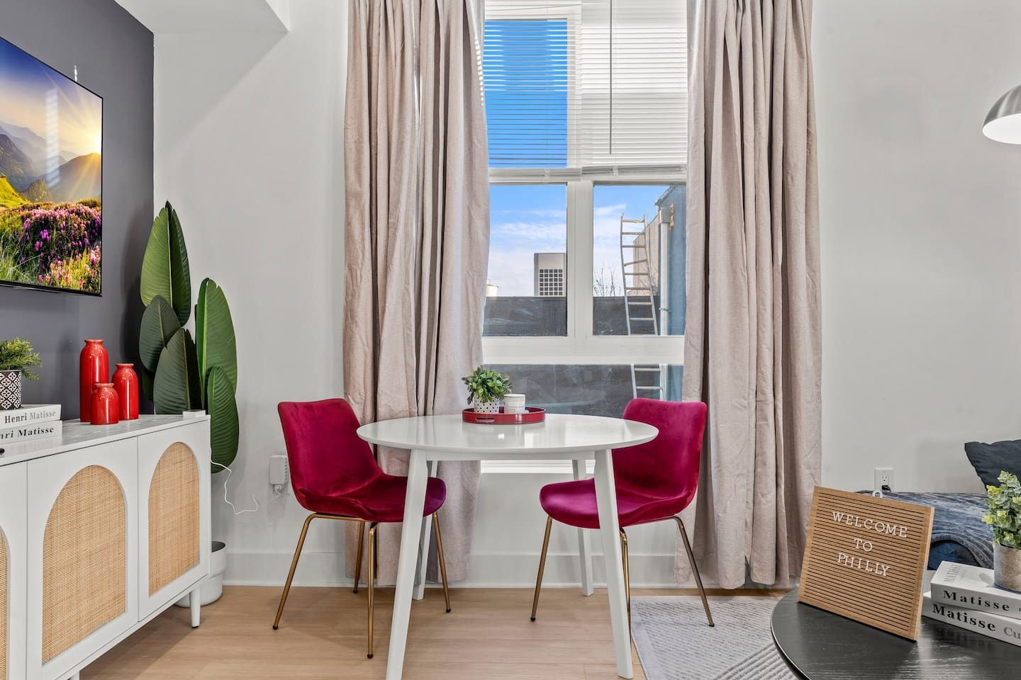 A modern room with a round table, two chairs, a cabinet with decorative items, and a window with curtains.