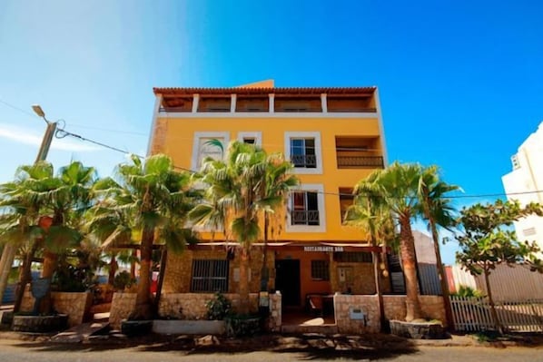 Un edificio de dos pisos con un restaurante en la planta baja, rodeado de palmeras.