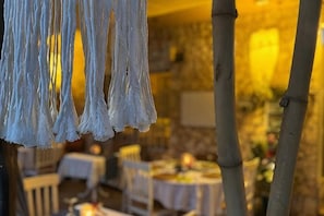 Un comedor con mesas y sillas, una lámpara colgante y una pared de piedra al fondo.
