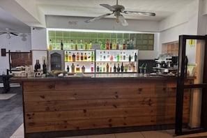 Zona de bar con mostrador de madera, estantes llenos de botellas y un ventilador de techo.