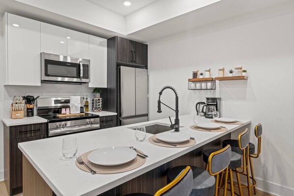 A modern kitchen with a central island, stainless steel appliances, and a bar area with stools.