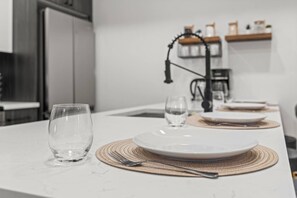 A dining table set with plates, cutlery, and glasses, with a kitchen in the background.