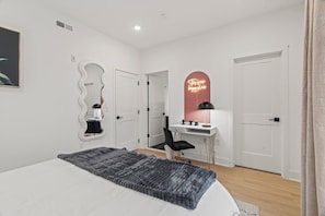 Un dormitorio con cama, escritorio, silla, espejo y letrero de neón.
