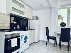 Una cocina moderna con estufa, microondas, refrigerador y lavadora. Cuenta con un comedor con mesa y sillas.
