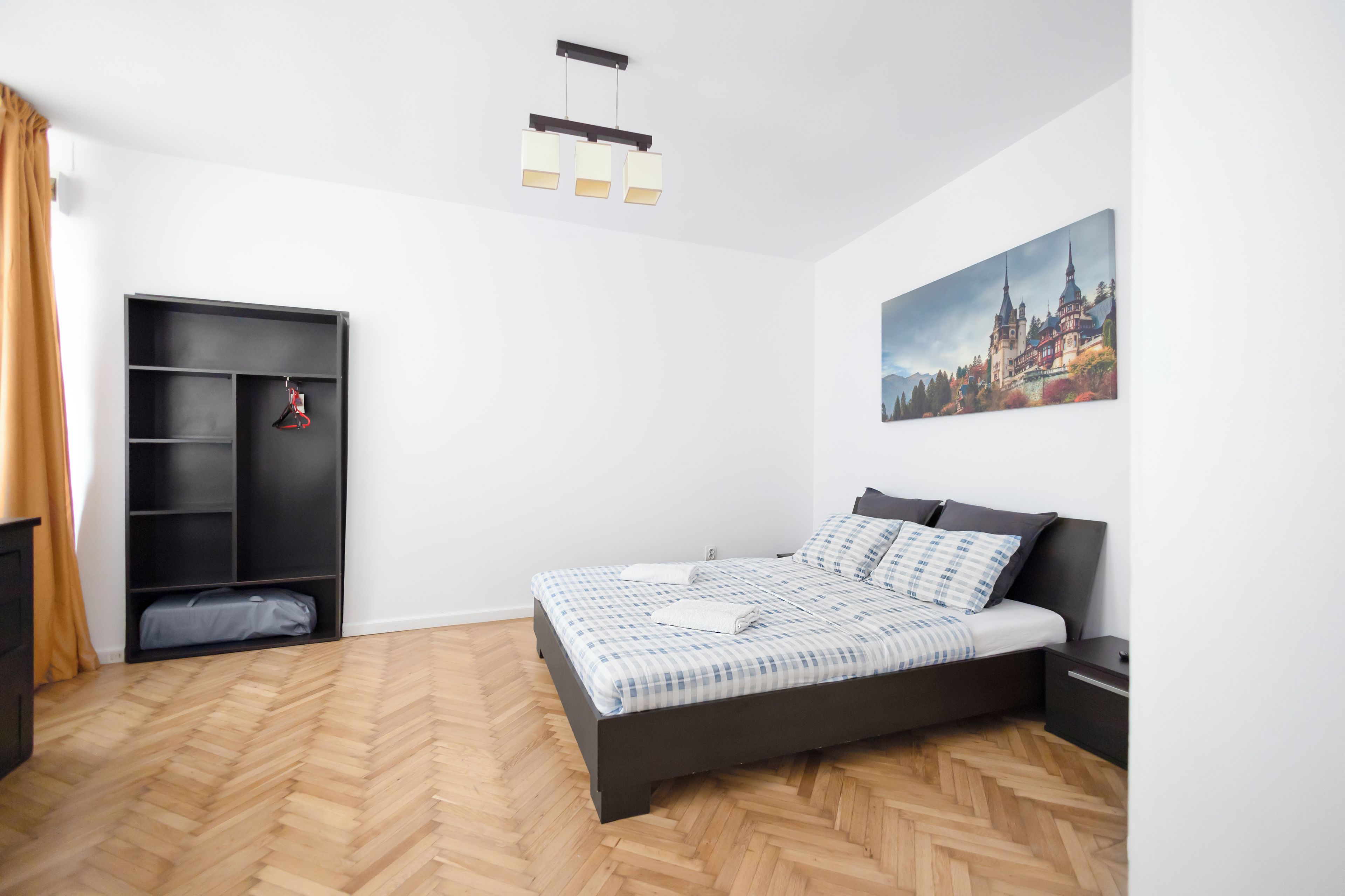Un dormitorio con una cama, un armario, un cuadro y un suelo con estampado de espiga.