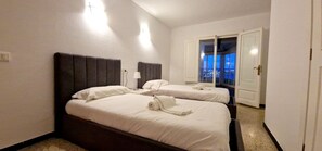 A hotel room with two beds, a nightstand, a lamp, and a view of the outside balcony. - Apartamento con Espectaculares Vistas (Palma de Mallorca)