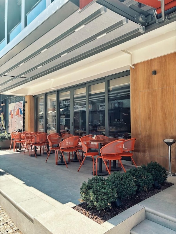 An outdoor seating area with tables and chairs, a wooden column, and a glass storefront. - Dugi (Istanbul)