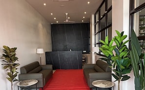 Zona de recepció amb catifa vermella, dos sofàs, una taula de recepció i una planta gran.