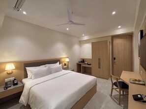 A hotel room with a bed, bedside lamps, a desk with a chair, a wardrobe, and a ceiling fan. - Mastiff Hotel, Hinjawadi (Paud)