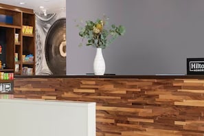 Balcão de recepção com painel de madeira, um vaso branco com folhagem e um letreiro 'Hilton Honors'.