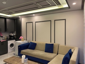 A modern living room with a beige sofa, a coffee table, and a washing machine in the background. - One Bedroom Apartment Near Beykent Metrobus Station (Istanbul)