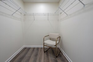 Un armario vestidor con estanterías metálicas, una silla y suelo de madera.