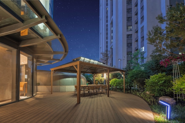 An outdoor deck with a wooden table and chairs, surrounded by greenery and a tall building in the background. - Holiday Inn Express Changchun Ecological Square (Changchun)