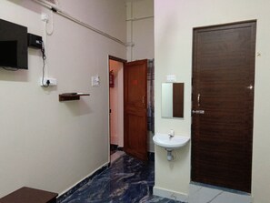 Un pasillo con suelo de mármol, una puerta de madera, un lavamanos blanco y un televisor montado.