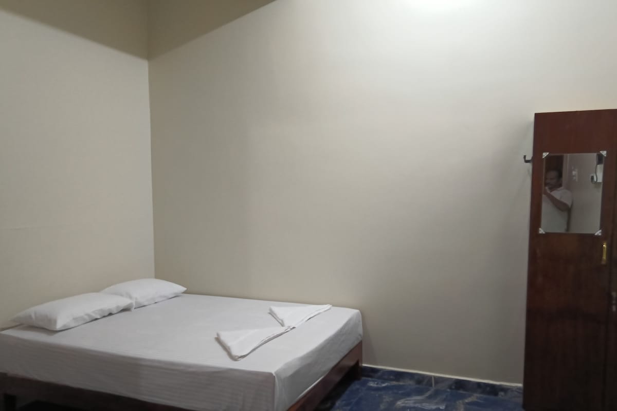 A single bed with white bedding in a room with a wooden wardrobe and a marble-patterned floor.