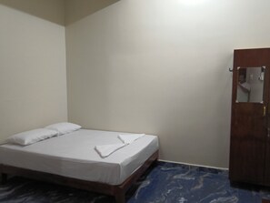 A single bed with white bedding in a room with a wooden wardrobe and a marble-patterned floor.