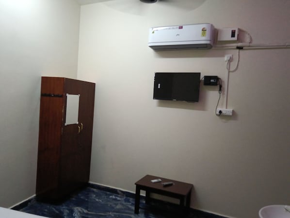 A room with a wooden door, a small table, a wall-mounted air conditioner, and a television.